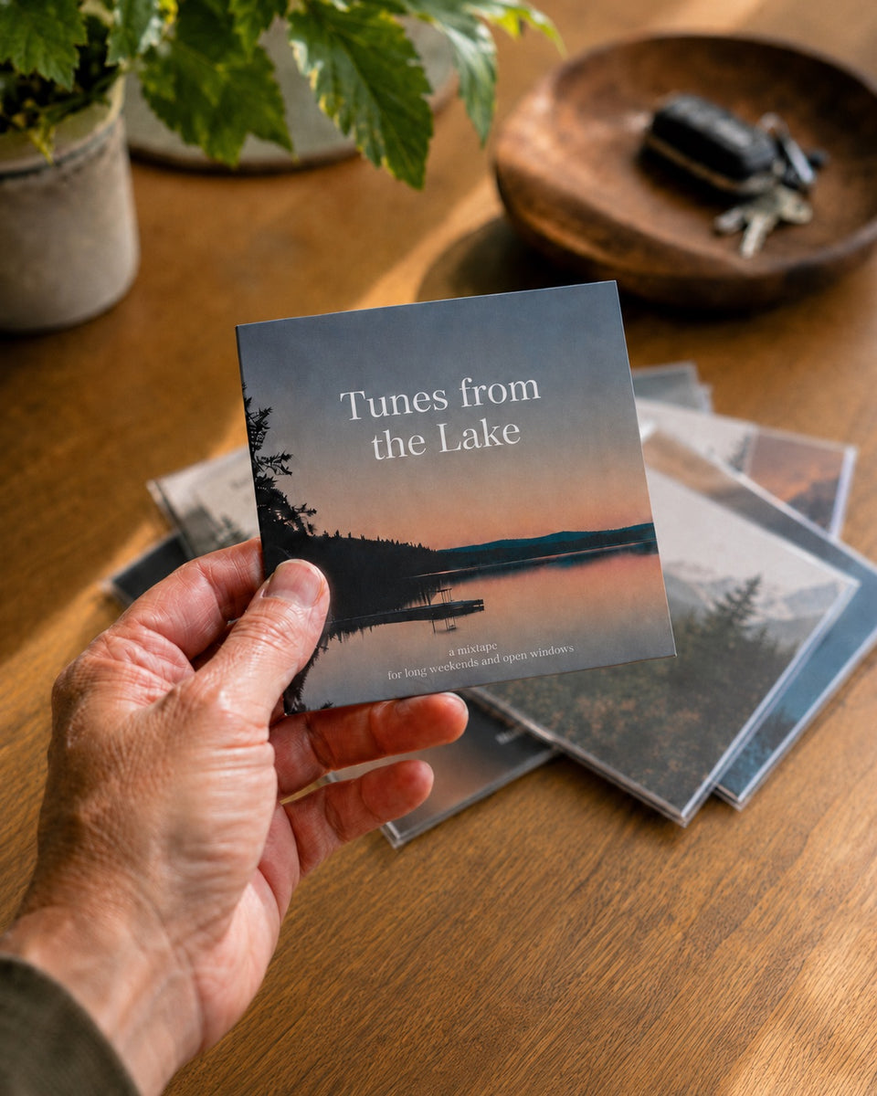 A hand holding a mix card titled “Tunes from the Lake” over a stack of cards on a wooden table